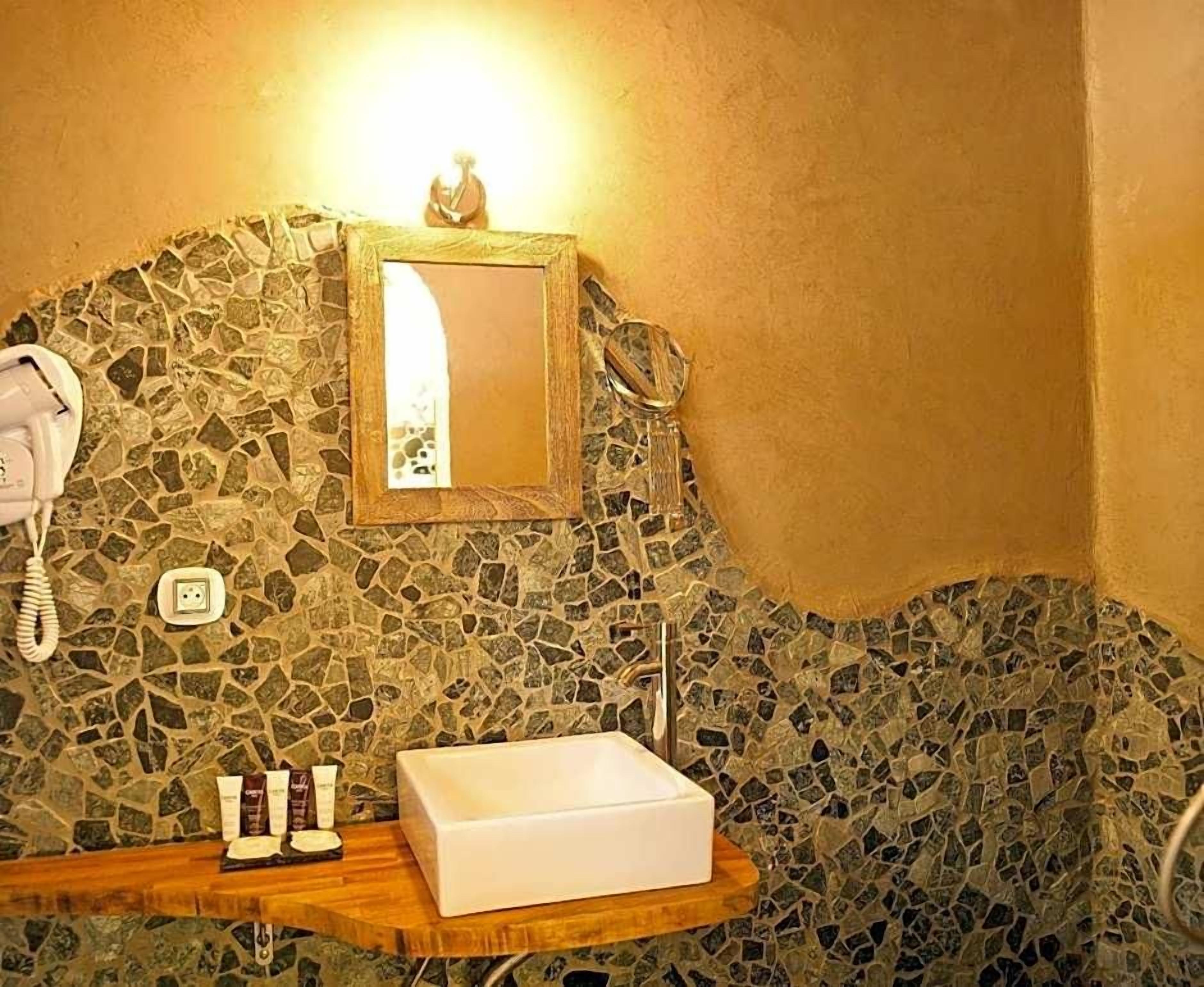 Une salle de bain avec un mur décoré de mosaïques, un lavabo blanc et un téléphone.