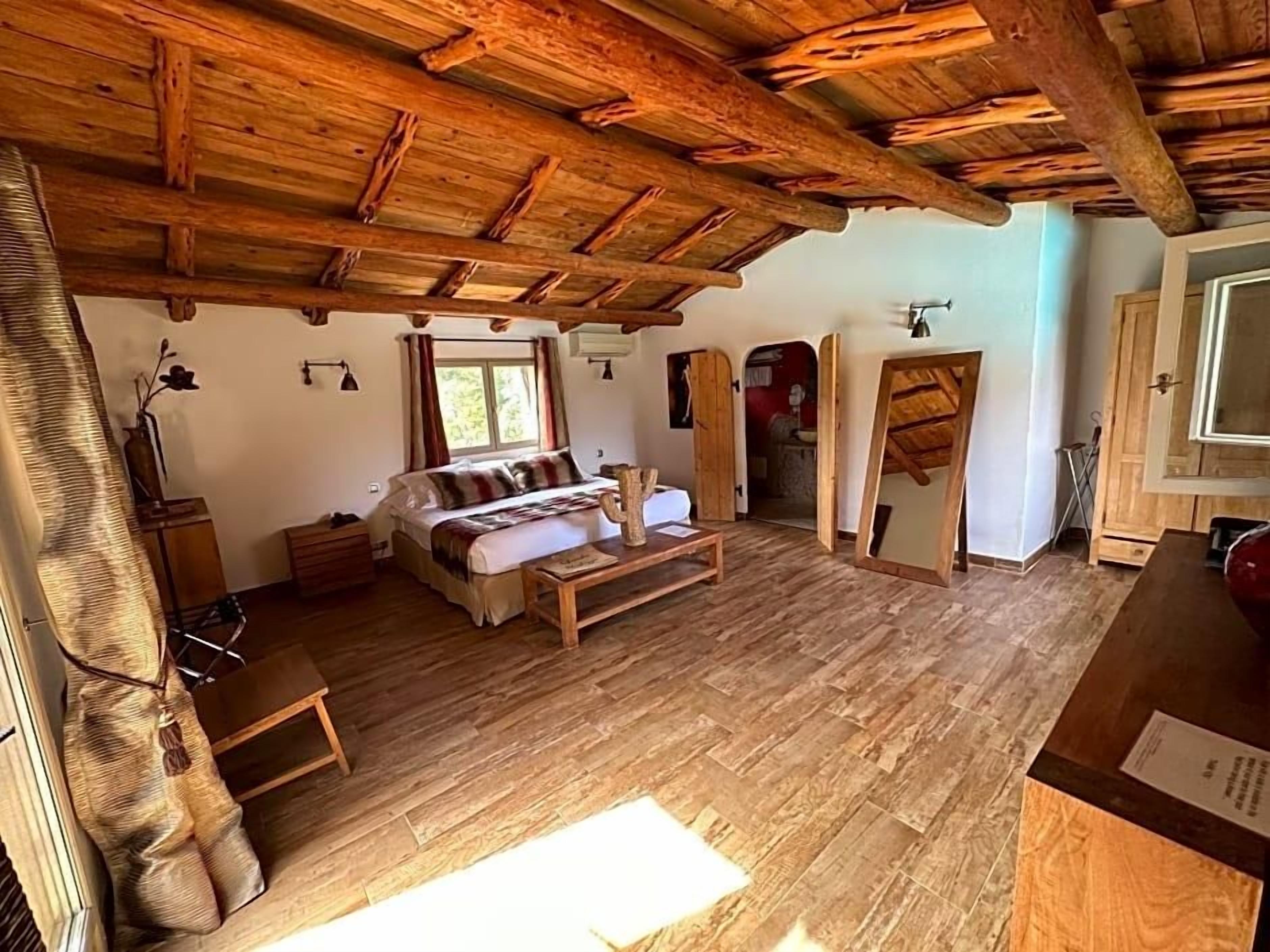 Une pièce rustique avec un plafond en bois, un canapé, une petite table et une fenêtre.