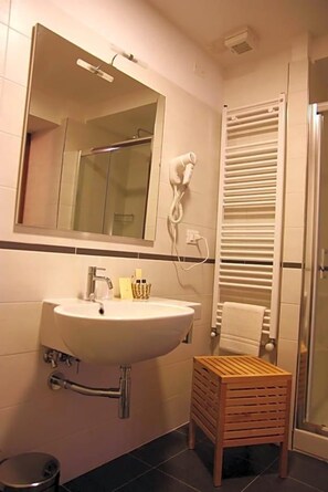 A bathroom with a sink, mirror, towel rack, and a small wooden stool. - Locanda Il Monastero (Luni)