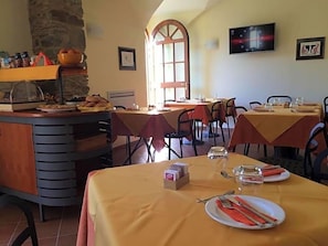 A dining area with tables set for meals, a buffet counter, and a stone wall. - Locanda Il Monastero (Luni)