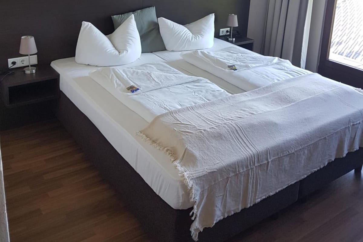 A hotel room with a large bed, a headboard, a nightstand with a lamp, and a window with curtains.