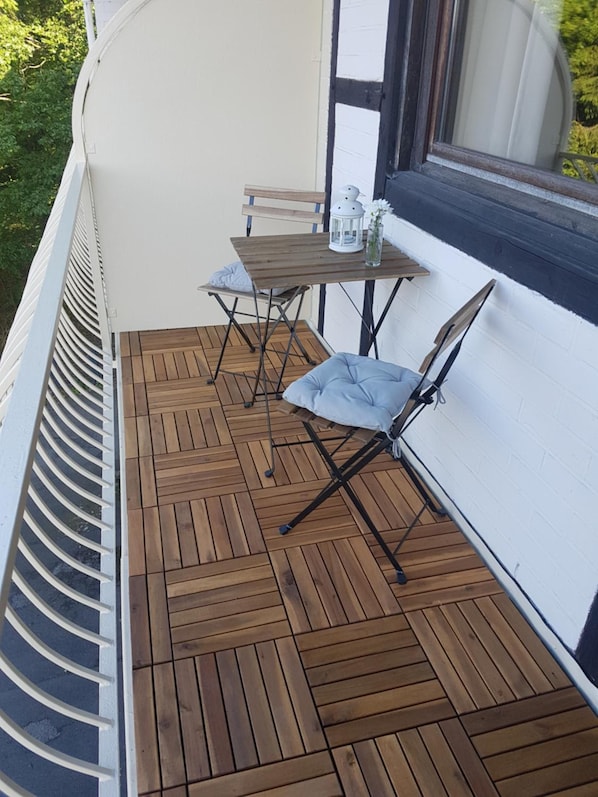 A wooden deck with a table and chairs, a lantern, and a window with a view of greenery. - Weltmann S Hotel Restaurant (Ennepetal)
