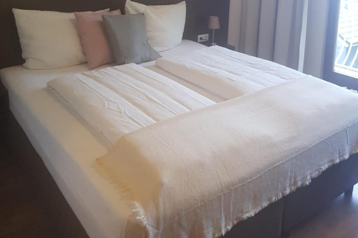 A hotel room with a large bed, a headboard, a nightstand, a lamp, a window with curtains, and a painting on the wall.