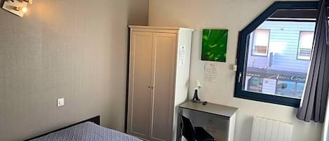 A hotel room with a bed, a desk, a wardrobe, a radiator, and a window with a view of the outside.