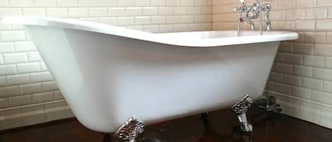 A freestanding bathtub in a corner with a white tiled wall and wooden floor.