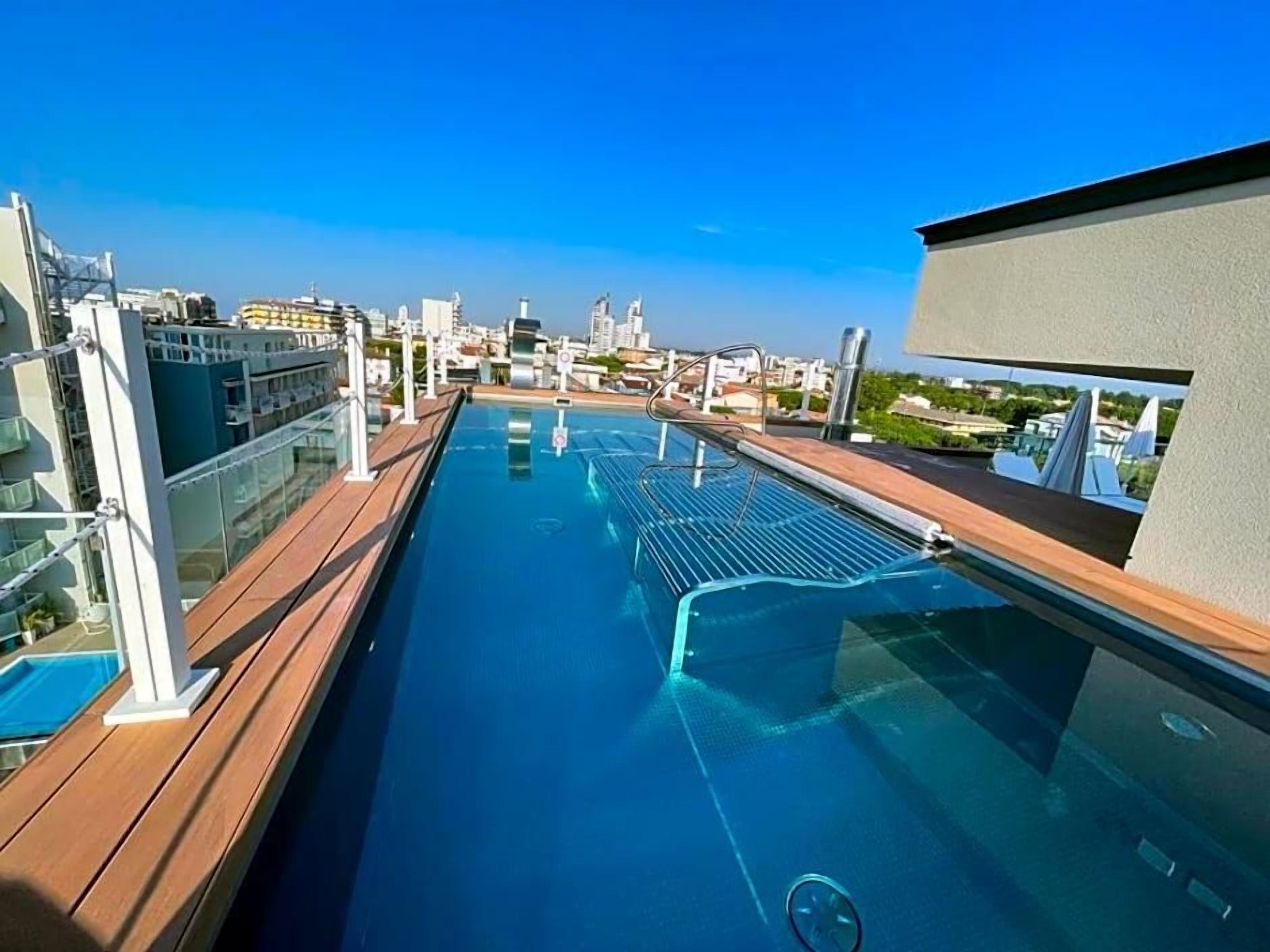 A rooftop pool with a city view, glass railings, and a clear sky.