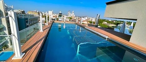 A rooftop pool with a city view, glass railings, and a clear sky.