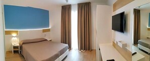 Une chambre d’hôtel équipée d’un lit, d’un bureau, d’un téléviseur à écran plat et d’une fenêtre avec des rideaux.