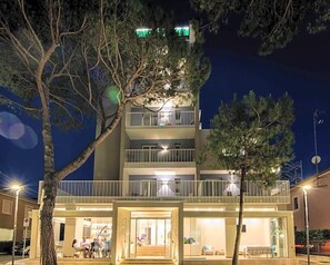Un hôtel à plusieurs étages doté de balcons, d’une entrée au niveau du sol et d’un espace extérieur aménagé avec des sièges, bien visible de l’extérieur.