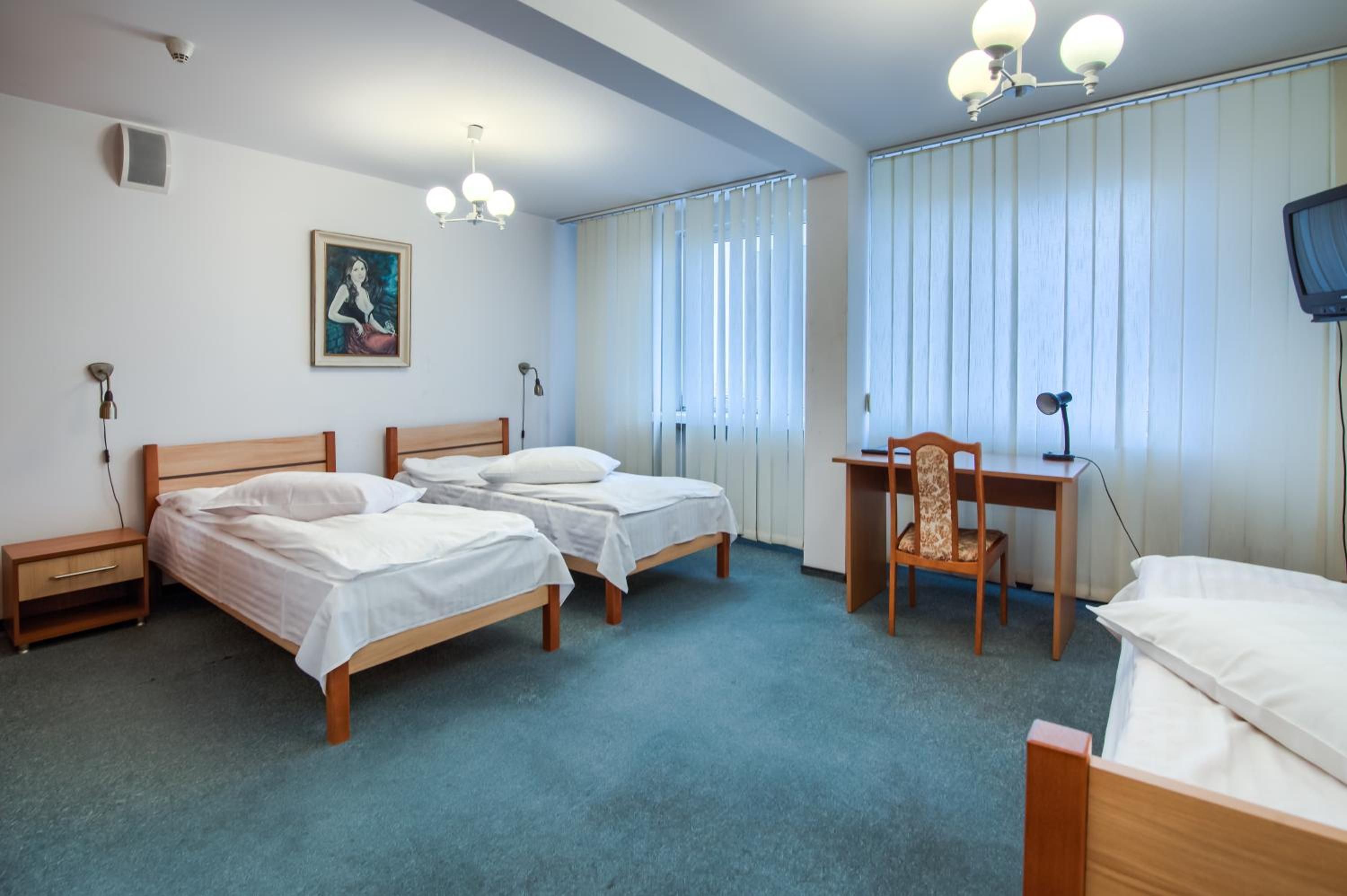 A hotel room with two single beds, a desk with a chair, a television, and a painting on the wall.