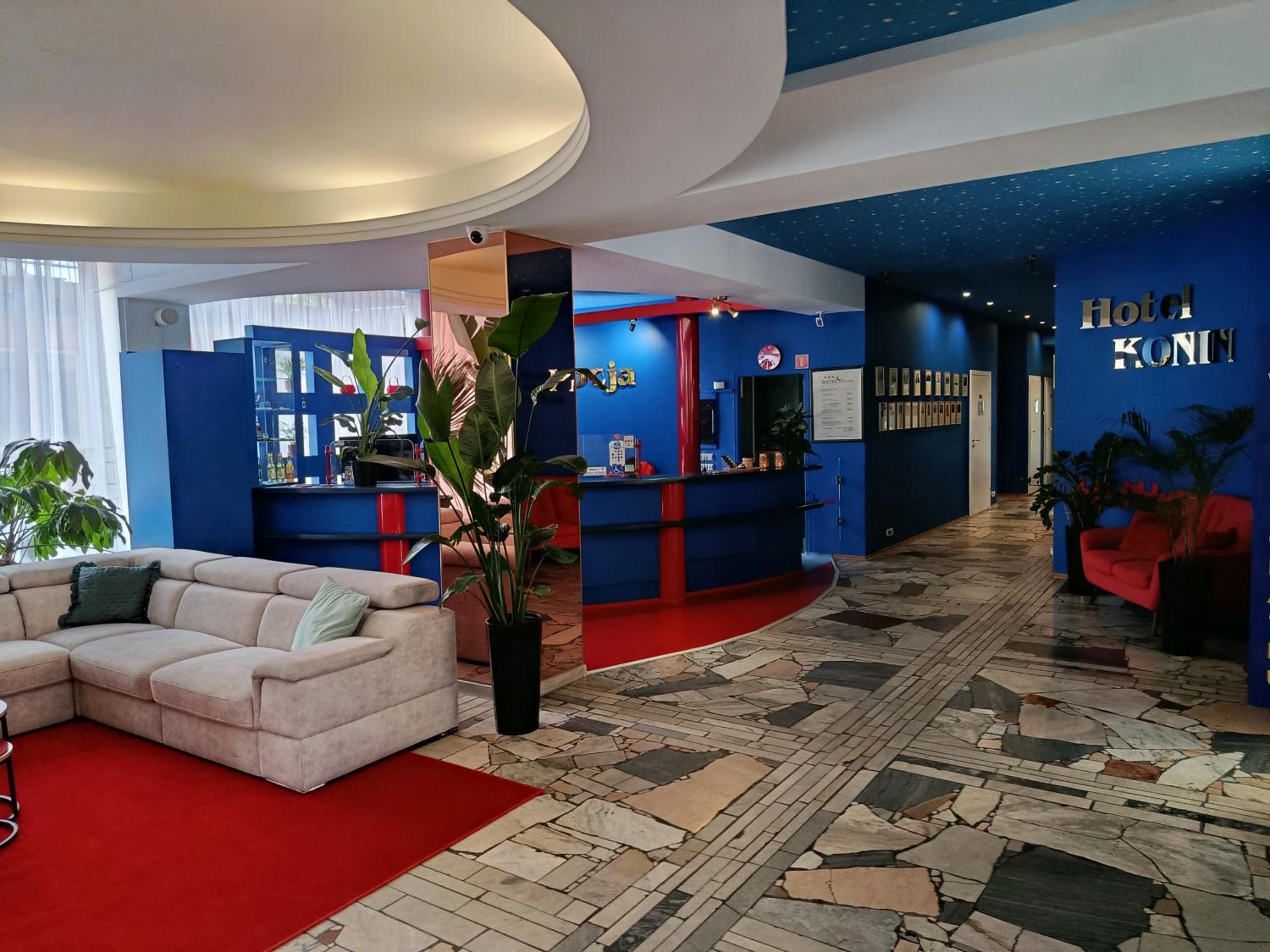 A hotel lobby with a curved reception desk, a seating area with a sofa, and a tiled floor.