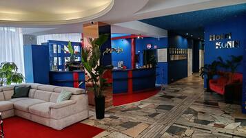 A hotel lobby with a curved reception desk, a seating area with a sofa, and a tiled floor.
