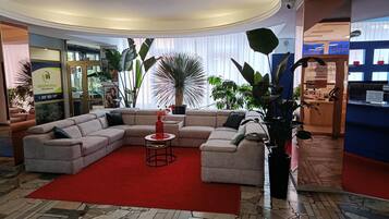 A modern living room with a sectional sofa, a red rug, and various plants.