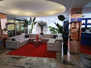 A modern living room with a sectional sofa, a red rug, and various plants.