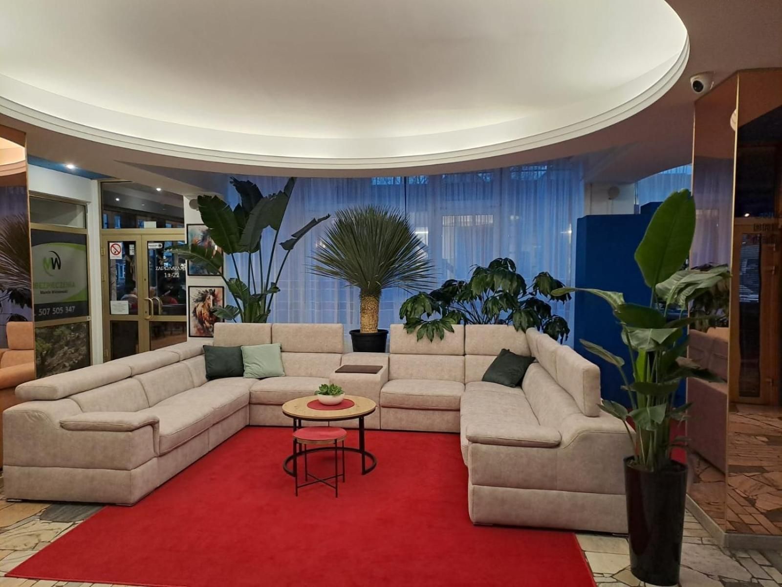 Una sala de estar moderna con un sofá seccional color beige, una mesita redonda con una planta y una alfombra roja.