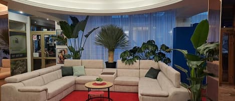 A modern living room with a beige sectional sofa, a small round table with a plant, and a red carpet.