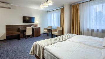 A hotel room with a bed, a desk, two chairs, a TV, and a window with curtains.