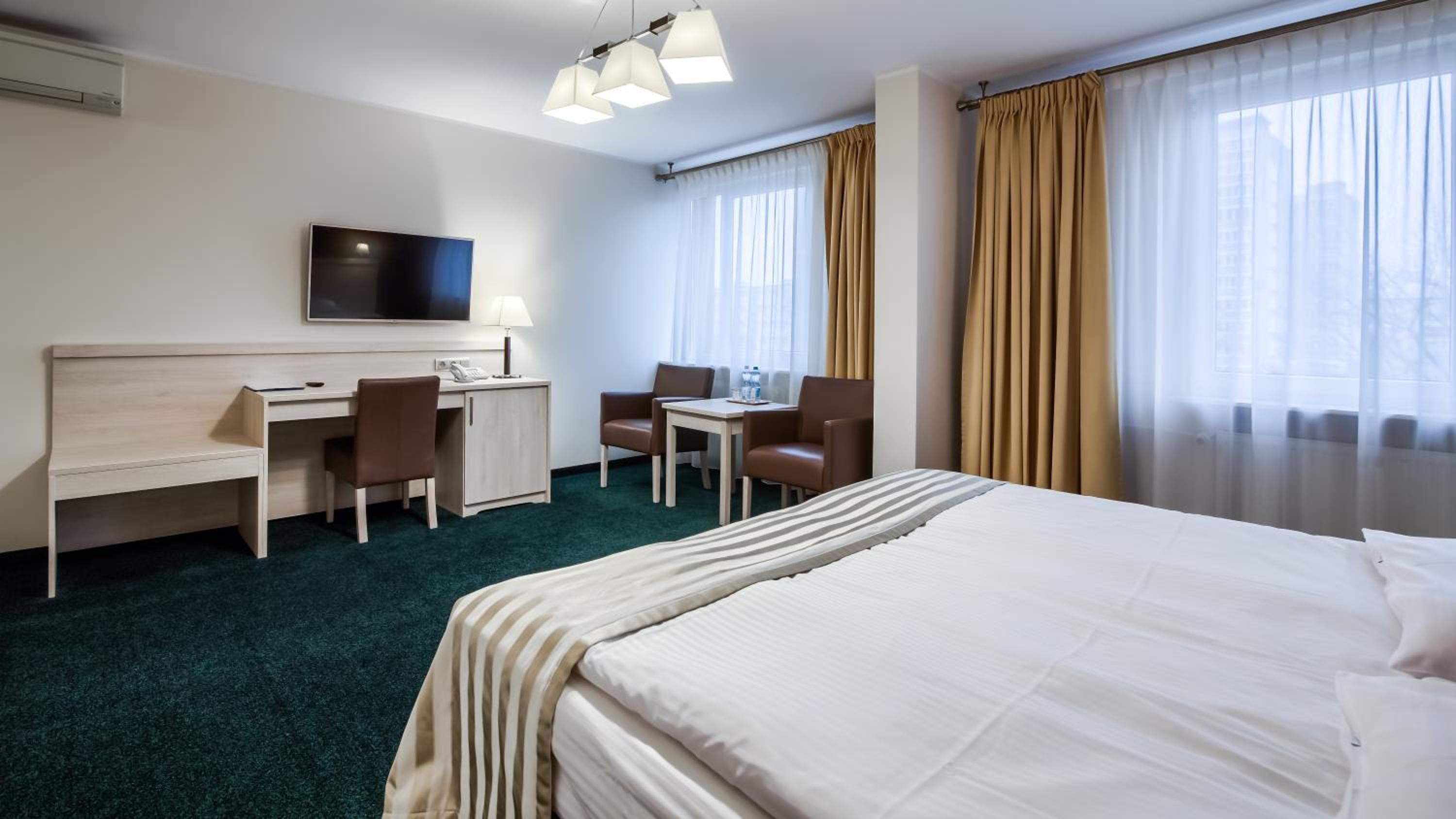 A hotel room with a bed, desk, chairs, a television, and curtains.