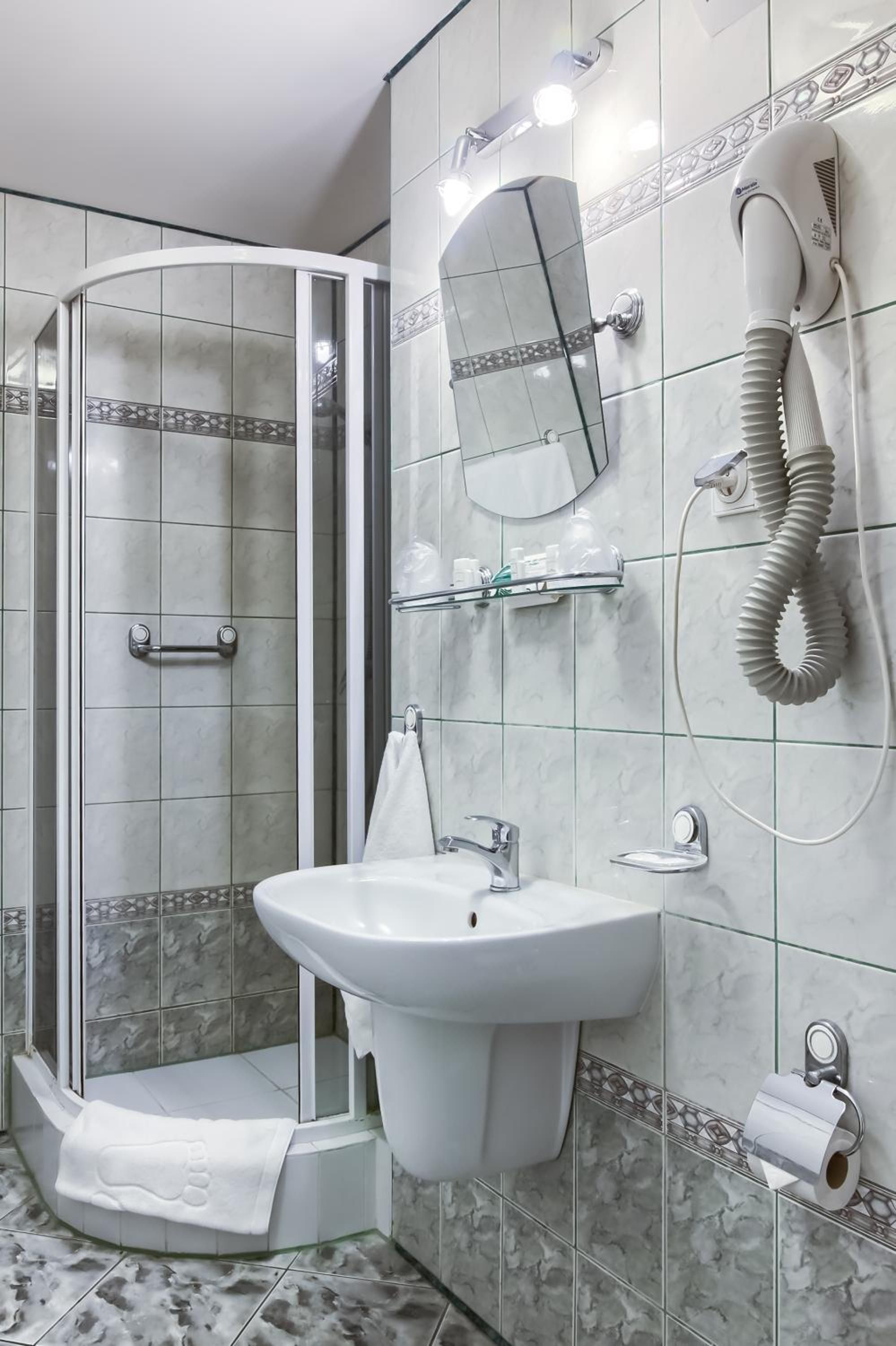 A bathroom with a glass shower enclosure, a sink, a mirror, and a hairdryer mounted on the wall.