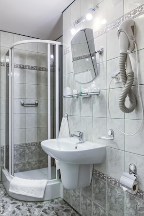 A bathroom with a glass shower enclosure, a sink, a mirror, and a hairdryer mounted on the wall.