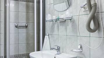 A bathroom with a glass shower enclosure, a sink, a mirror, and a hairdryer mounted on the wall.