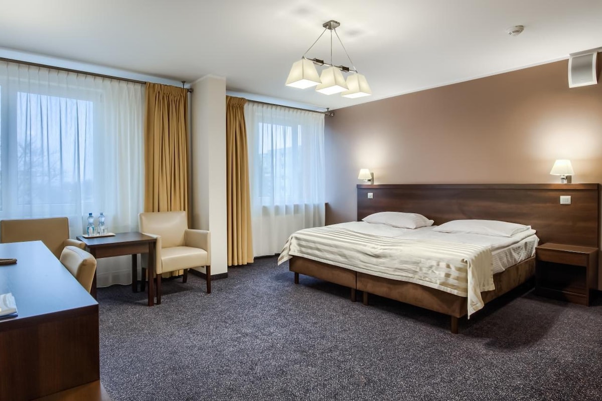 A hotel room with a bed, a desk with a telephone, a chair, and a lamp.