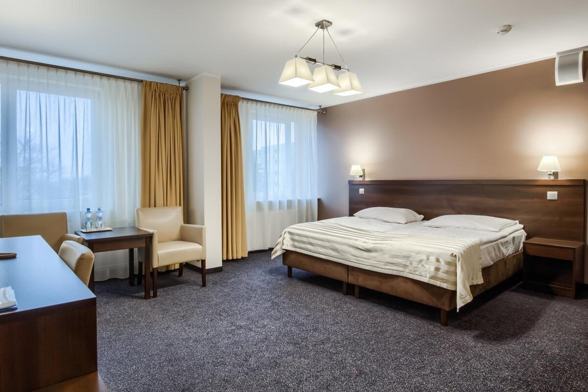 A hotel room with a bed, a desk with a telephone, a chair, and a lamp.