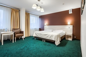A hotel room with a bed, a desk, a chair, a nightstand, and a lamp.