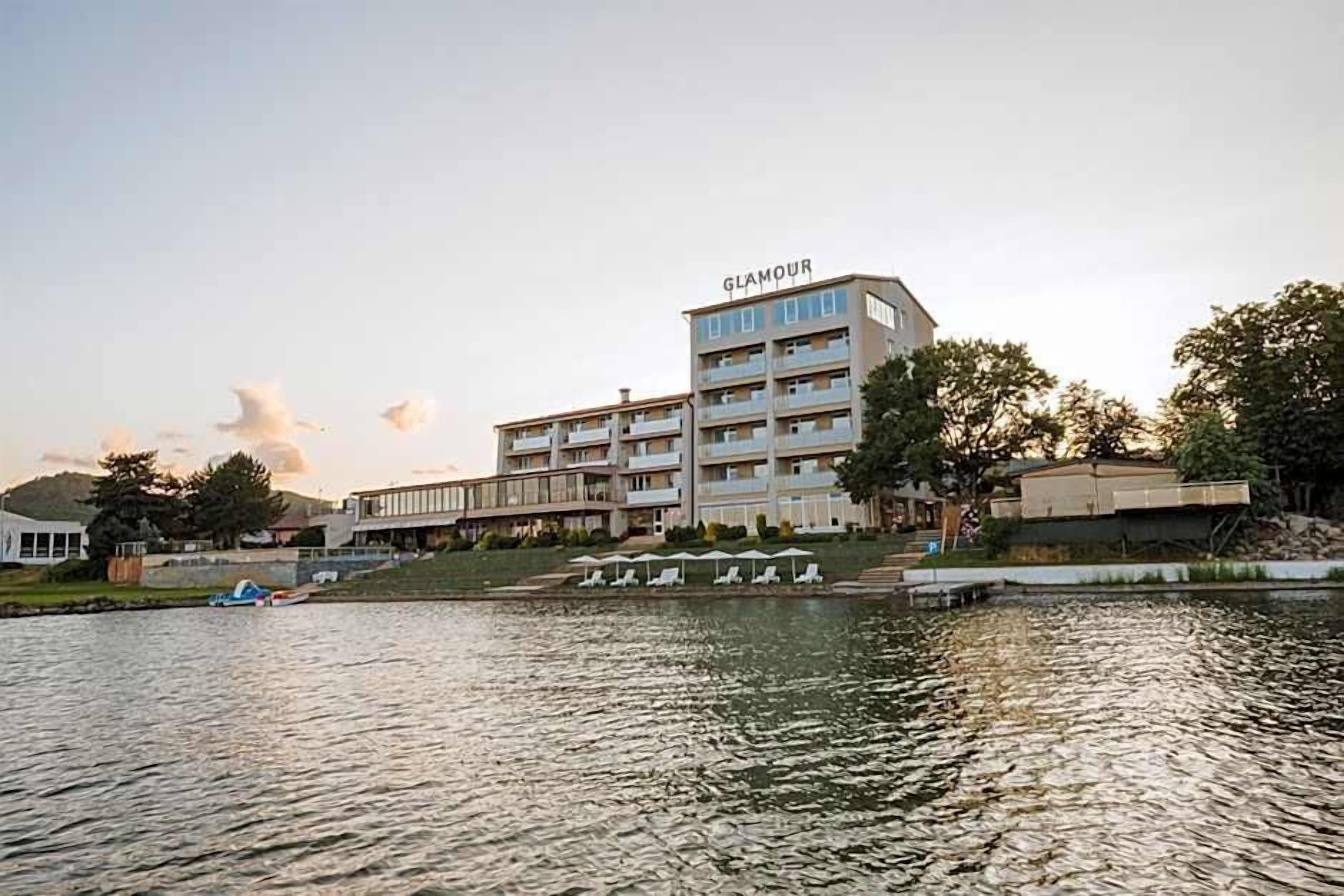 A multi-story hotel with a visible name sign, a waterfront location, and a pool area with lounge chairs.