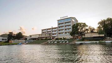 A multi-story hotel with a visible name sign, a waterfront location, and a pool area with lounge chairs.