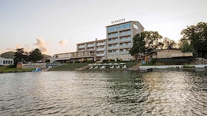 A multi-story hotel with a visible name sign, a waterfront location, and a pool area with lounge chairs.