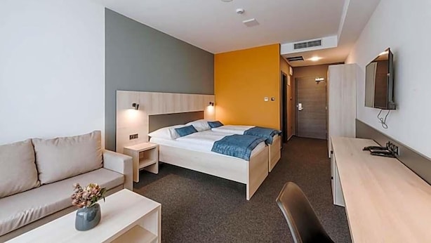 A hotel room with a bed, a desk, a chair, a sofa, and a TV.