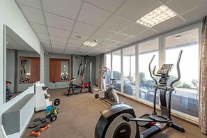 A gym with cardio equipment, weightlifting stations, and a large window providing a view of the outside.