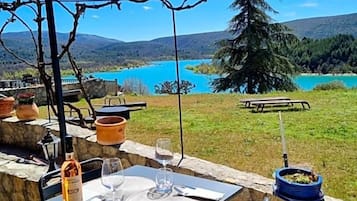Un espace de restauration en plein air avec une table dressée pour deux personnes, offrant une vue panoramique sur un paysage magnifique, avec un lac et des montagnes.