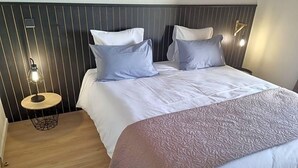 Quarto com cama, duas mesas de cabeceira, luminária na parede e colcha estampada.