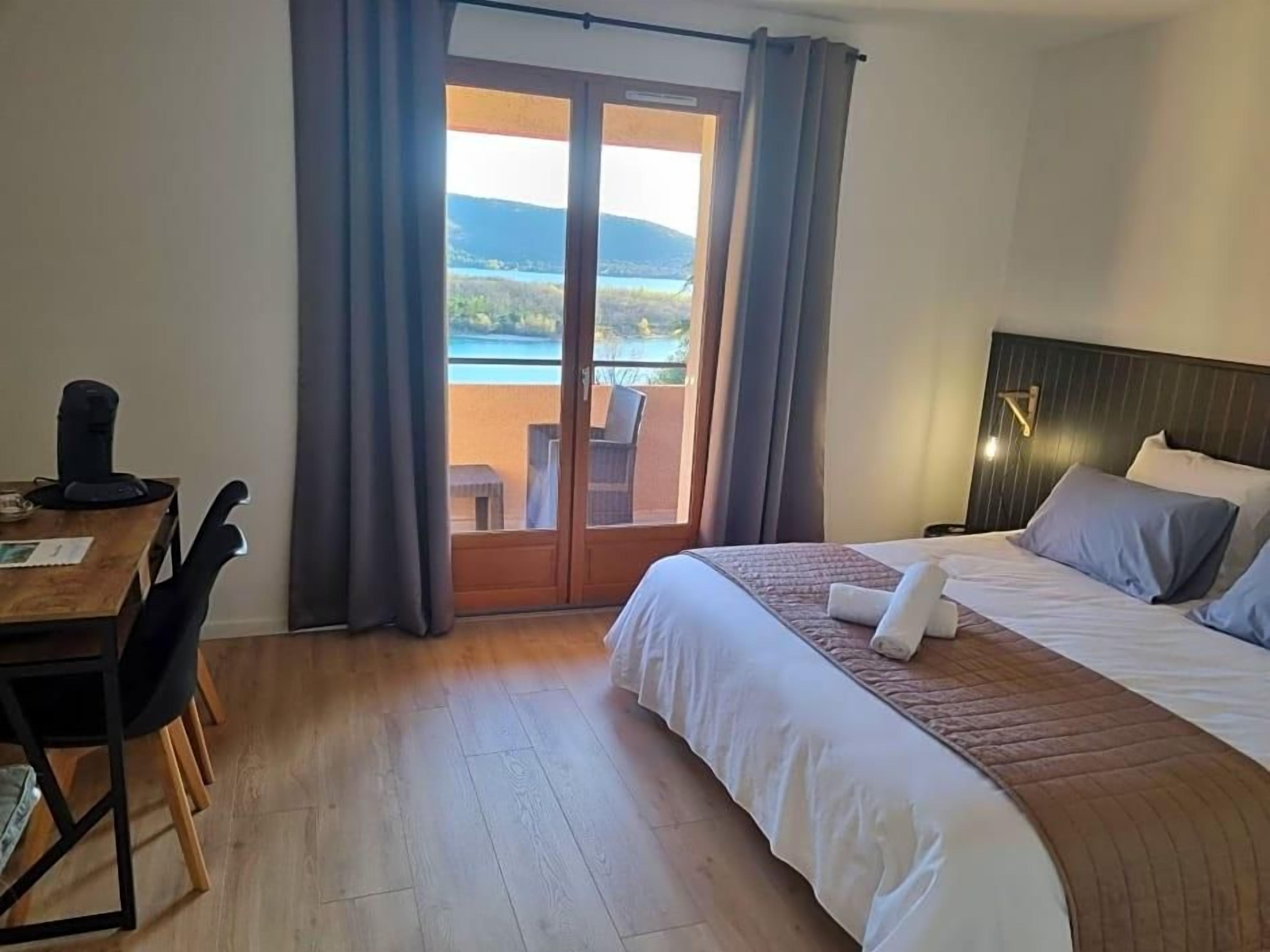 Een hotelkamer met een bed, een bureau en uitzicht op een wateroppervlak via een schuifdeur.