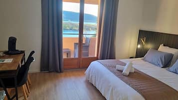 Une chambre d’hôtel avec un lit, un bureau et une vue sur un plan d’eau, accessible par une porte coulissante.