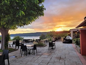 An outdoor seating area with tables and chairs, overlooking a body of water and hills during sunset. - Auberge Des Salles (Les Salles-sur-Verdon)