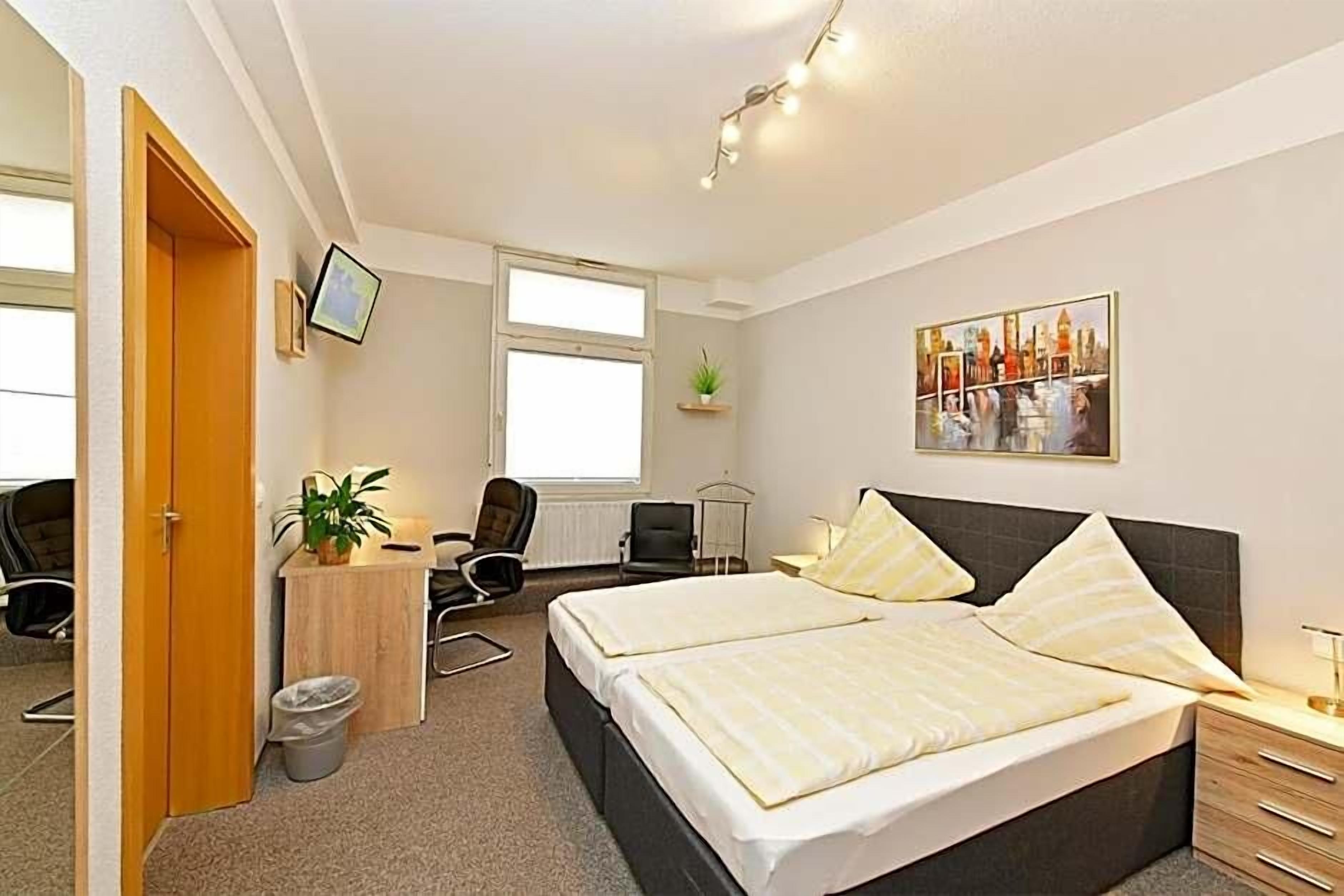 A hotel room with a bed, desk, chair, and a small plant.