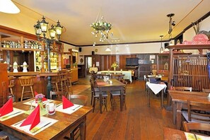 Ein Restaurant mit Holztischen und -stühlen, einem Barbereich mit Flaschenregalen und einer Kristallleuchter.