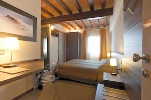 A hotel room with a bed, bedside table, lamp, and a desk with a chair.