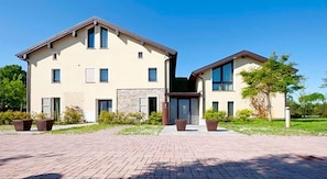 A two-story residential building with a brick driveway and potted plants.