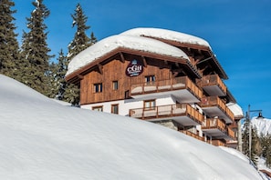Un edificio de madera de varios pisos con balcones, rodeado de laderas nevadas y árboles.