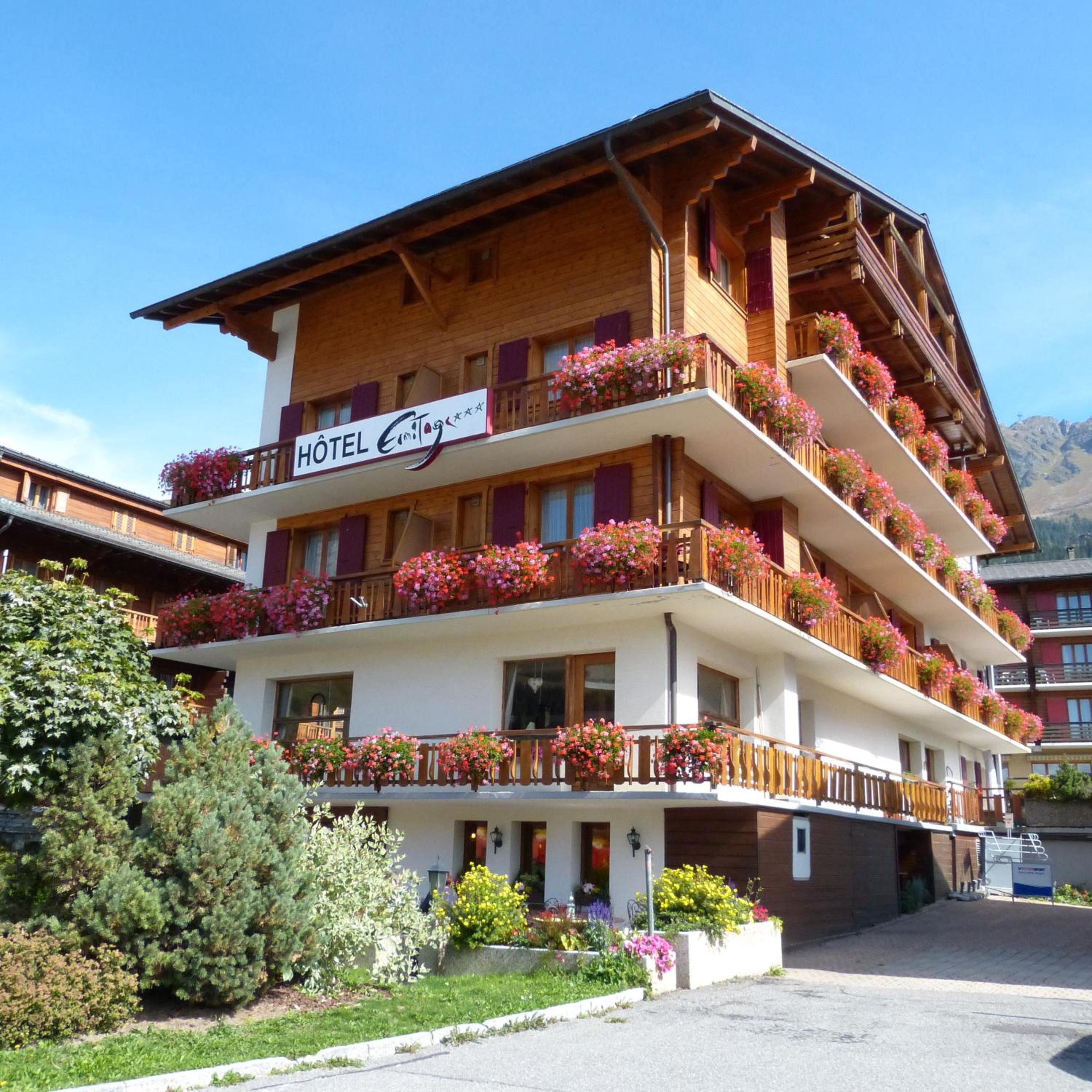 A multi-story hotel with balconies adorned with flowers, a clear sky, and mountains in the background.