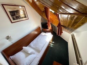 Una cama individual con sábanas blancas en una habitación con vigas de madera en el techo y un cuadro en la pared.