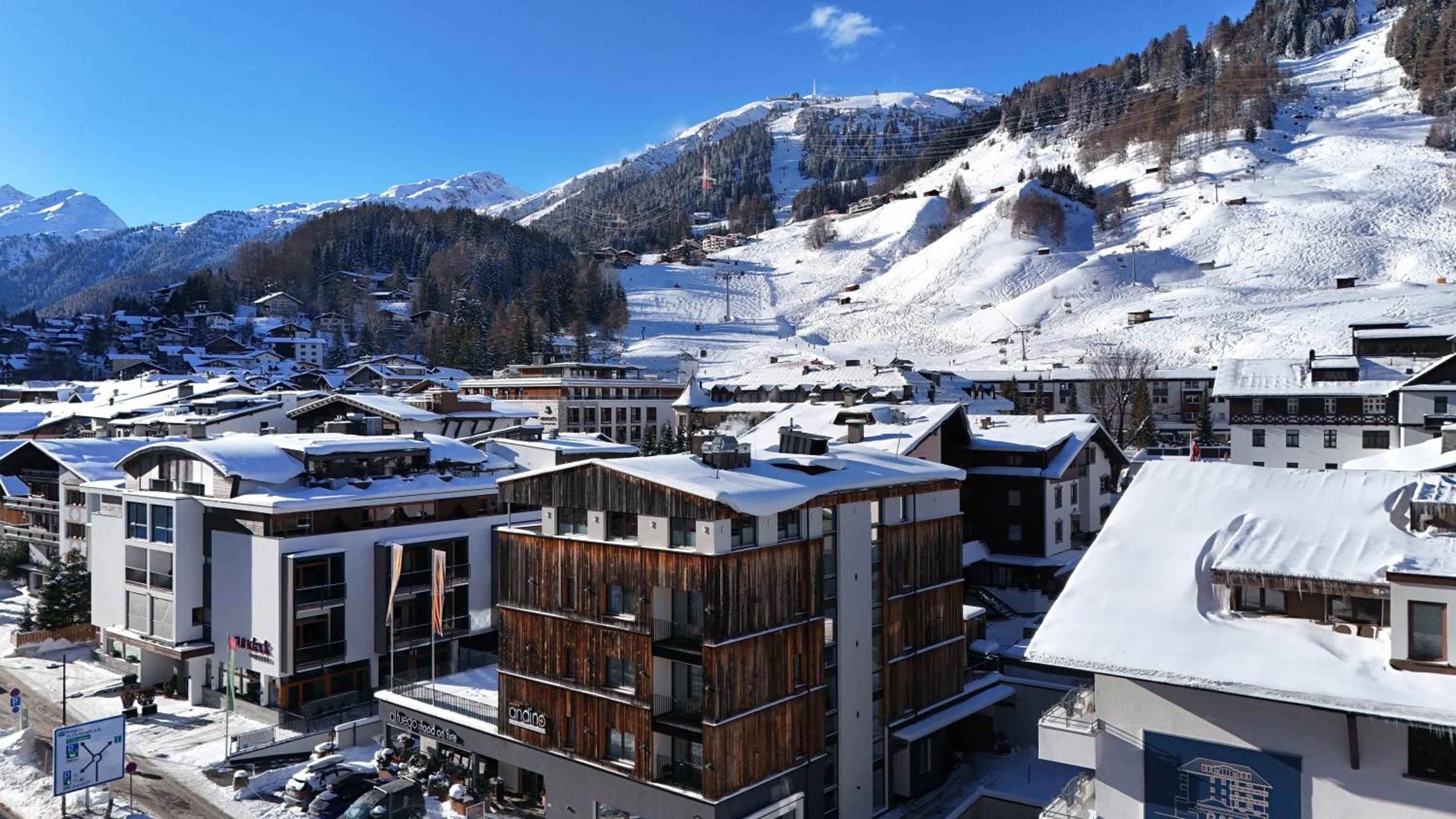 A snow-covered mountain town with modern buildings, ski slopes, and a clear blue sky.