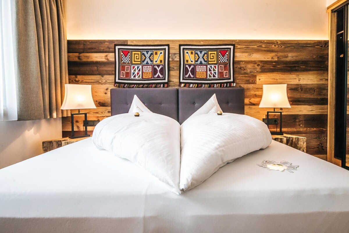 A hotel room with a large bed, two wall-mounted lamps, and a wooden wall with a patterned tapestry.