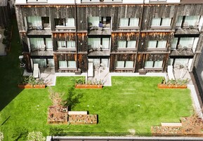 A multi-story building with balconies, a well-maintained lawn, and planters.