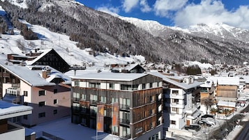 Un pueblo de montaña cubierto de nieve con edificios modernos, incluyendo un hotel y un telesilla al fondo.