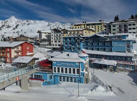 Un pueblo cubierto de nieve en la montaña, con diversos edificios, incluyendo un edificio azul destacado con el letrero 'Snow White Mountain Spa'.
